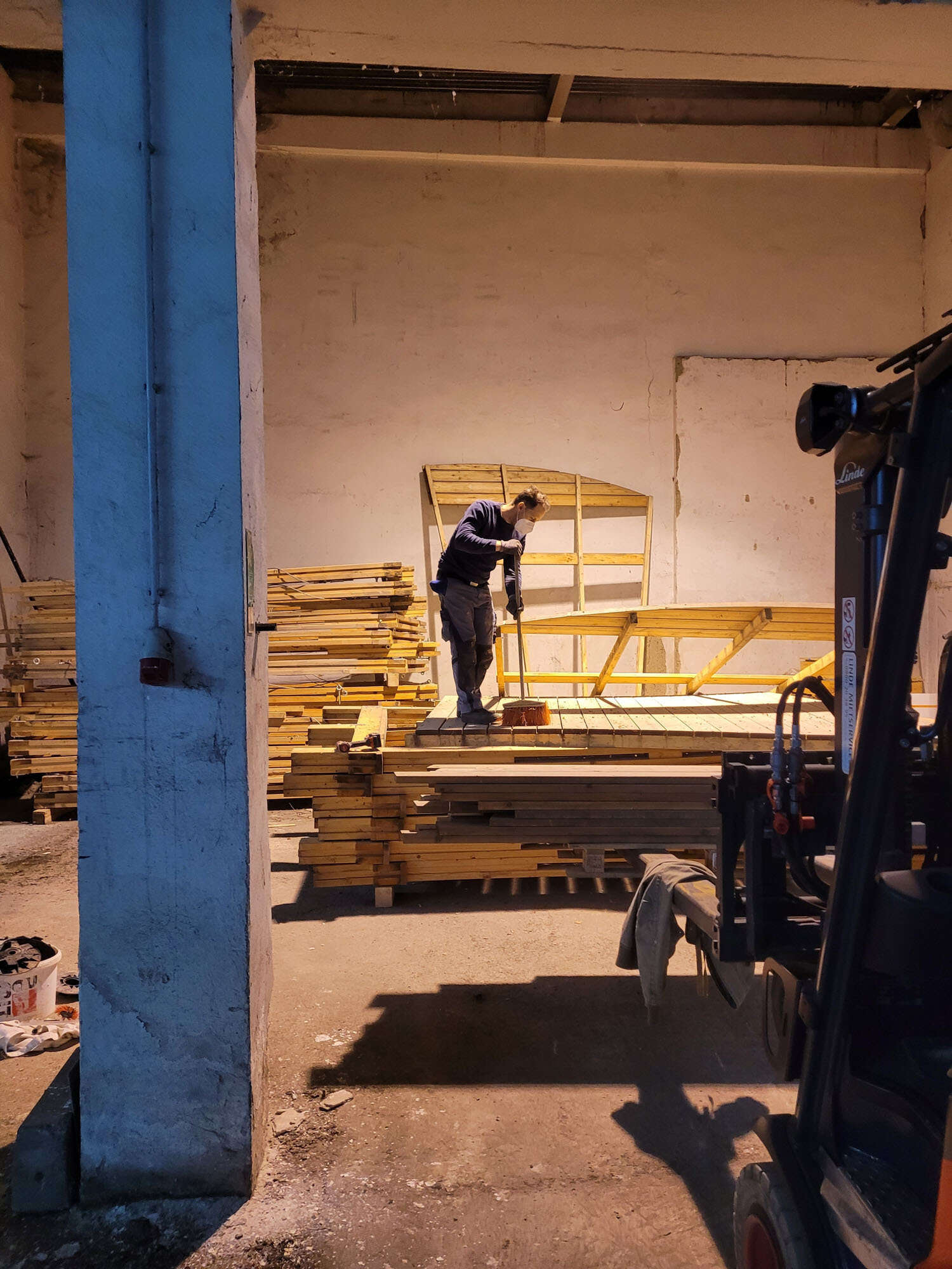 Jemand steht in einer Garage und kehrt über eine Holzpalette.